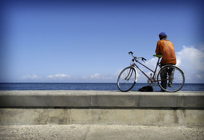 Rear view of man cycling by sea against clear sky