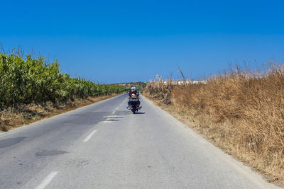 Man riding motorcycle with woman on road against clear blue sky