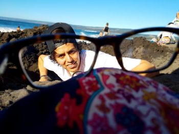 Portrait of young man seen through eyeglasses on rocky shore