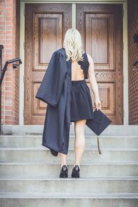 Rear view of woman holding mortarboard while standing on steps