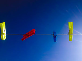 Low angle view of multi colored clothespins against clear blue sky