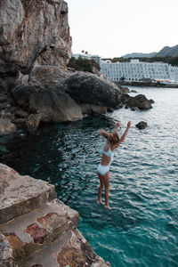 Young girl jumps from the rocks into the sea
