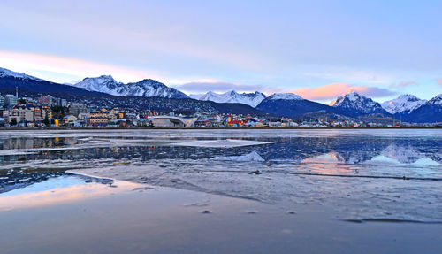 Scenic view of river by snowcapped mountains against sky during sunset