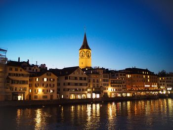 River by illuminated buildings against clear blue sky