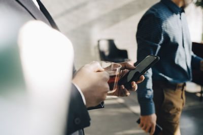 Midsection of businessman using mobile phone while having tea at office