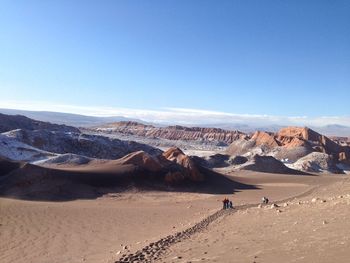 People walking on barren landscape against blue sky