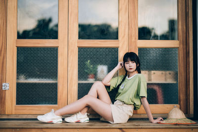 Portrait of young woman sitting on window