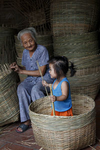 Grandmother looking at granddaughter playing in wicker basket