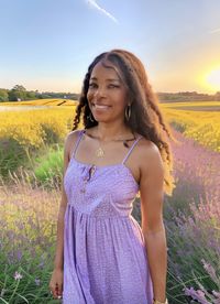 Young woman standing on field against sky during sunset