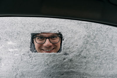 Portrait of smiling mid adult man looking through snow covered window