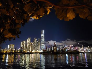 Illuminated buildings by river against sky at night