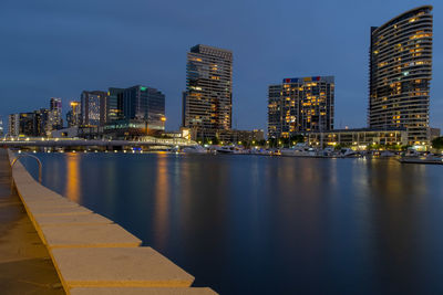 Illuminated buildings by river against sky at night