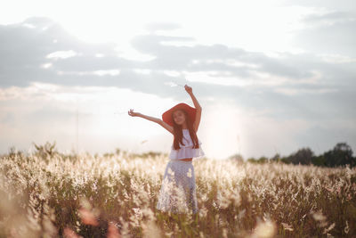 Portrait cute girl with arms raised standing amidst plants on field against sky