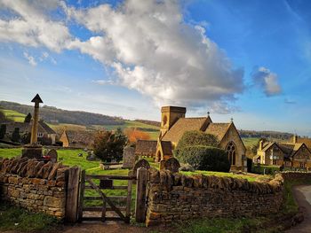 Plants growing on old building by field against sky
