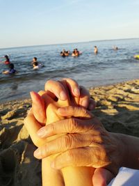 Close-up of couple holding hands by sea against sky