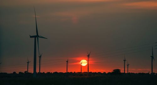 Silhouette of wind turbines on field against sky during sunset