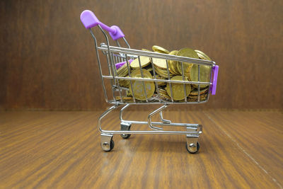 Close-up of coins in shopping cart on wooden table