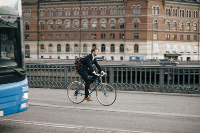 Full length of businessman riding bicycle on road in city