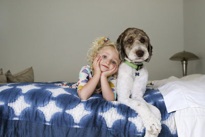 Portrait of girl with dog lying on bed against wall