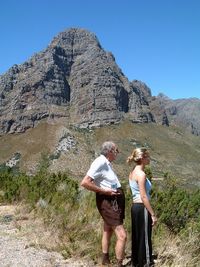 Side view of grandfather and granddaughter standing on rock against clear sky