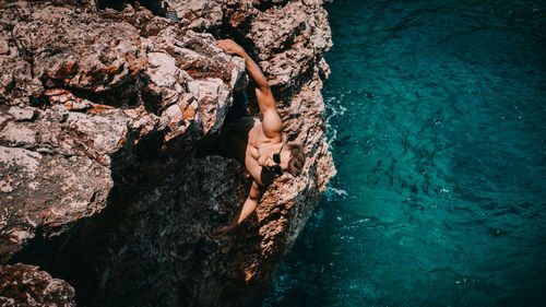High angle view of man climbing rock formation by sea