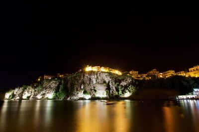 Illuminated city by river against sky at night