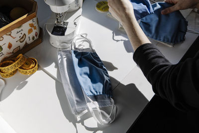 Crop woman tailor making protective masks with fabric at home workshop