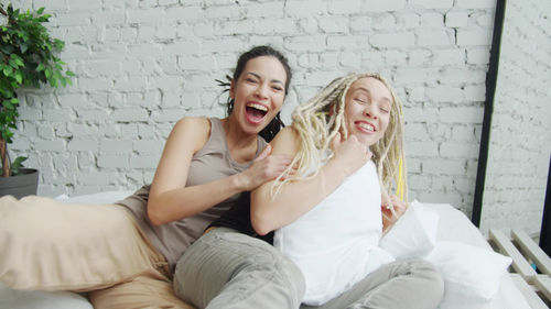 Woman smiling while sitting on bed against wall