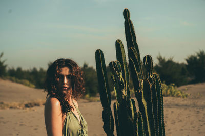 Portrait of young woman on cactus at beach against sky