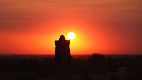 Silhouette built structure against orange sky