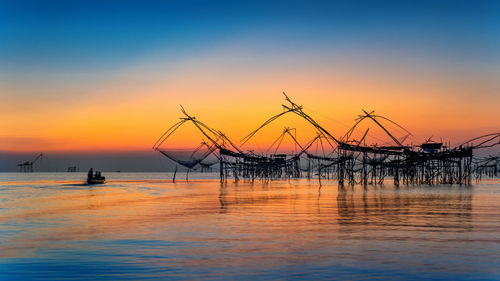 Silhouette cranes against sea during sunset