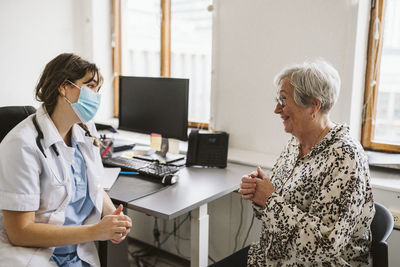 Smiling senior female patient talking with medical expert wearing face mask