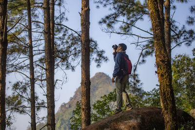 Rear view of young man standing against trees in forest