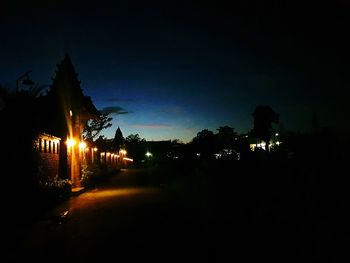 Illuminated street amidst buildings against sky at night