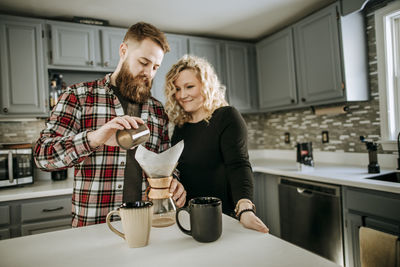 Man with beard and woman make over coffee together in their kitchen