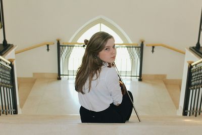 High angle view of teenage girl with violin while sitting on steps at home