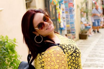 Portrait of cheerful young woman wearing sunglasses while standing on footpath