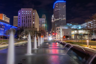 Illuminated street amidst buildings in city at night