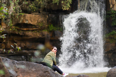 Side view of woman wearing sunglasses against waterfall