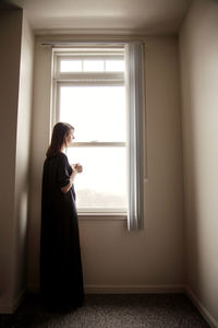 Side view of woman looking away while standing by window at home