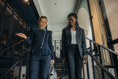 Mature businesswoman discussing with female colleague while moving down from steps in hotel