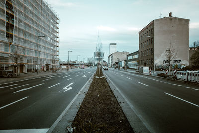 Road by cityscape against sky
