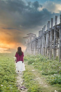 Rear view of woman standing on field against sky during sunset