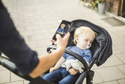 Hand of father photographing sleeping son on baby stroller in city