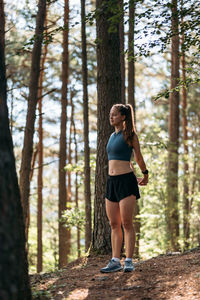 Young female runner stretching and warming up before running at morning forest trail.
