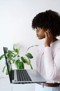 Black woman with afro hair with ear buds earphones holding laptop during video conference