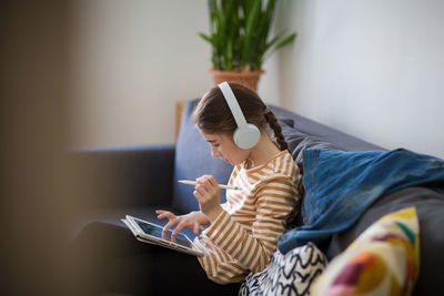 Side view of girl using digital tablet while sitting on sofa