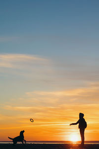 Silhouette of a man and a dog on the sea against the sunset. nature walk of a woman with a pet