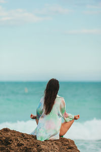 Rear view of woman sitting on beach against sky