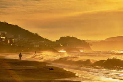 Silhouette person on beach against sky during sunrise